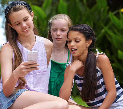 Buy stock photo A young girl showing her friends something on a cellphone while they're sitting outside