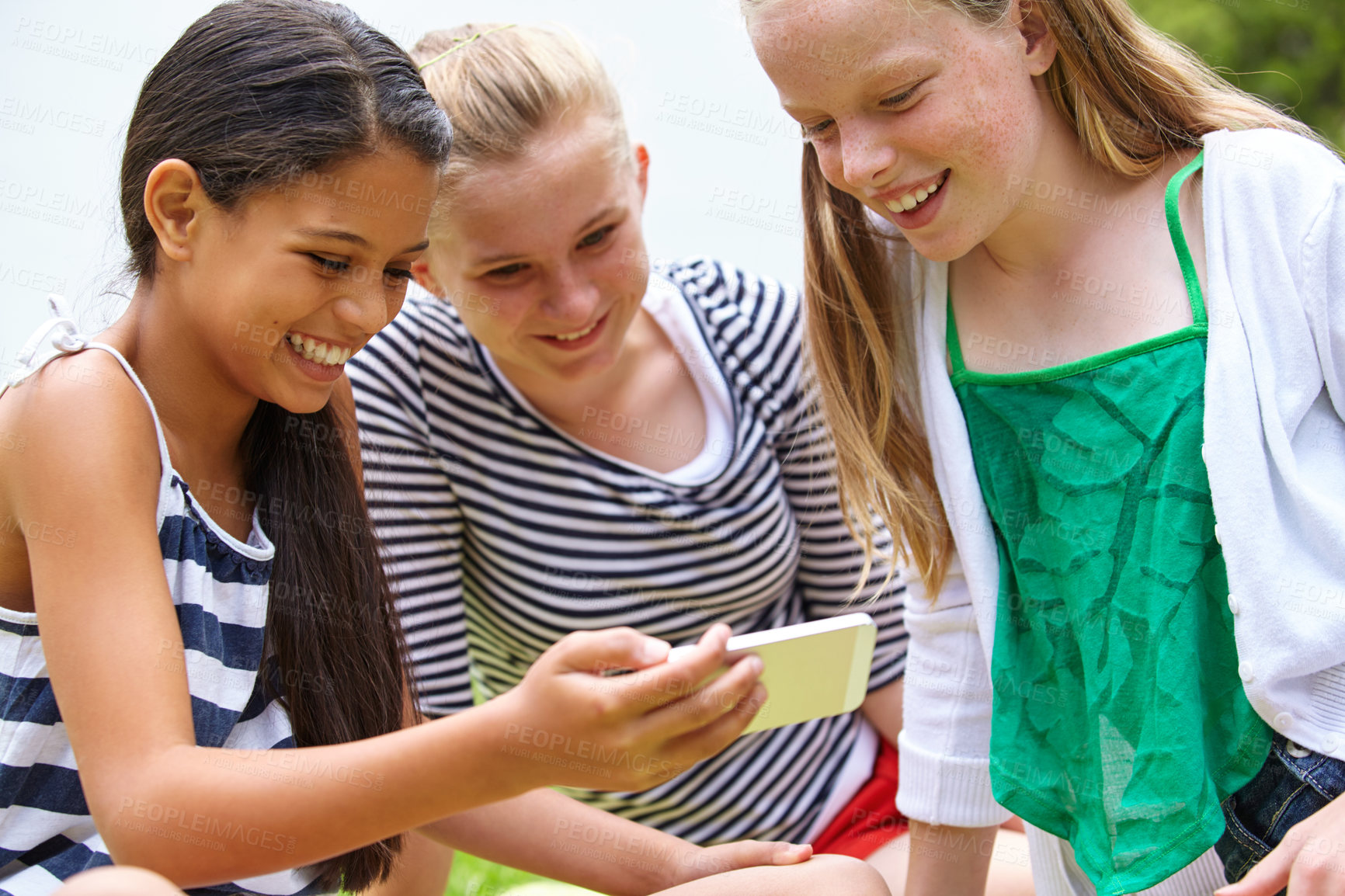 Buy stock photo A young girl showing her friends something on a cellphone while they're sitting outside