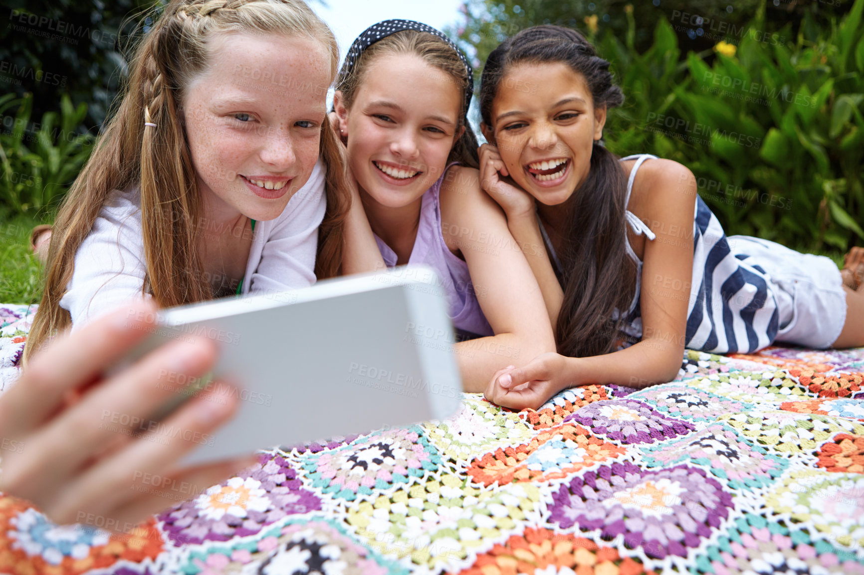 Buy stock photo Shot of a group of young girls taking a selfie together while lying on a blanket outside