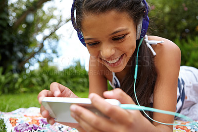 Buy stock photo Shot of a young girl listening to music on her cellphone in the outdoors