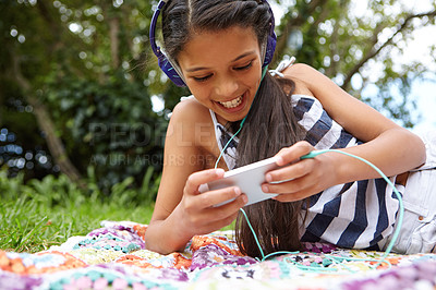 Buy stock photo Shot of a young girl listening to music on her cellphone in the outdoors