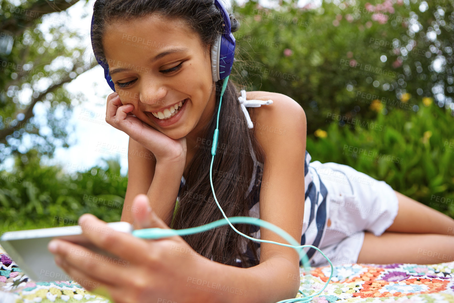 Buy stock photo Shot of a young girl listening to music on her cellphone in the outdoors