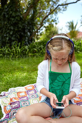 Buy stock photo Shot of a young girl listening to music on her cellphone while sitting outside