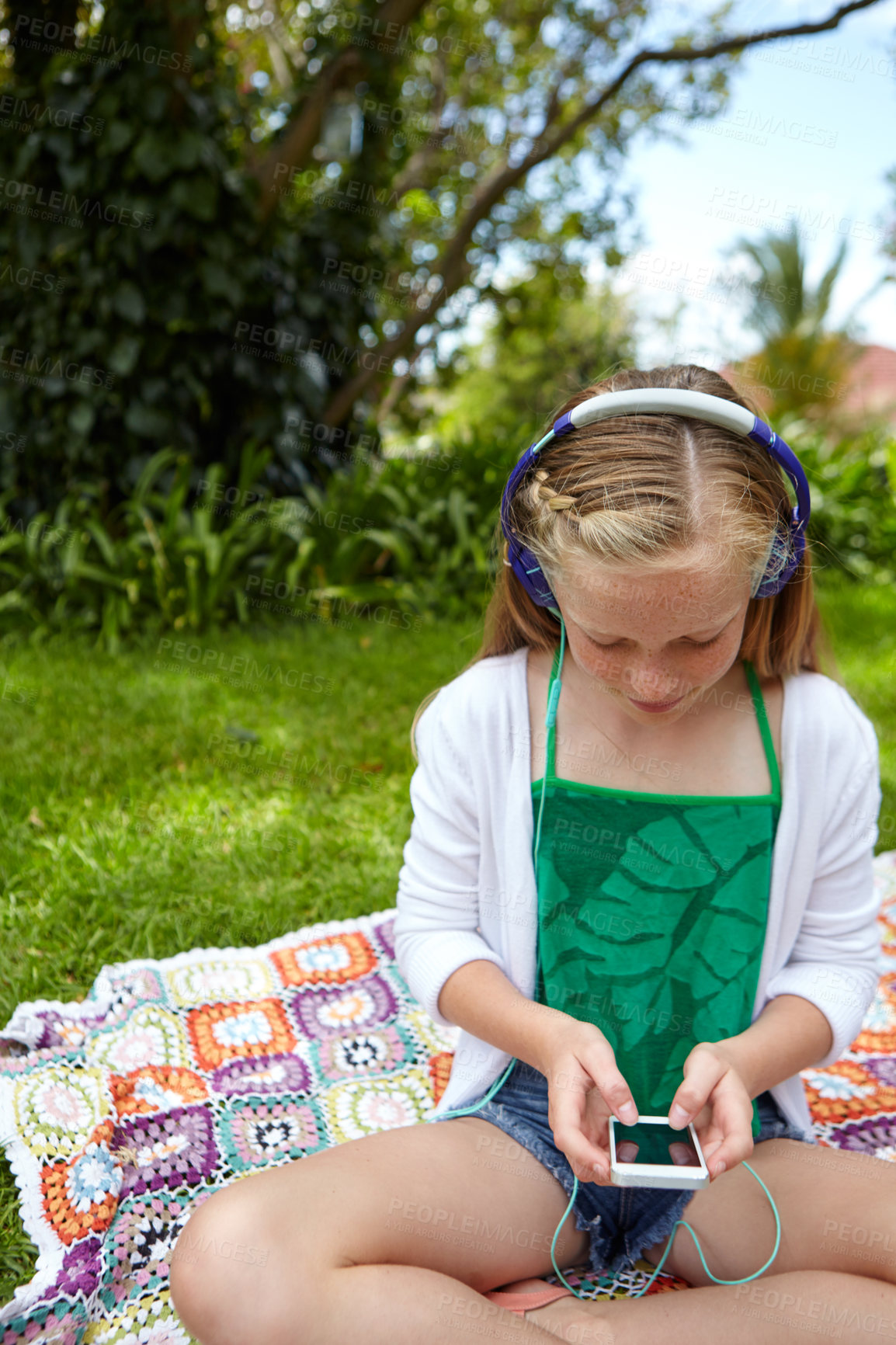 Buy stock photo Shot of a young girl listening to music on her cellphone while sitting outside