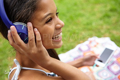 Buy stock photo Shot of a young girl listening to music on her cellphone while sitting outside