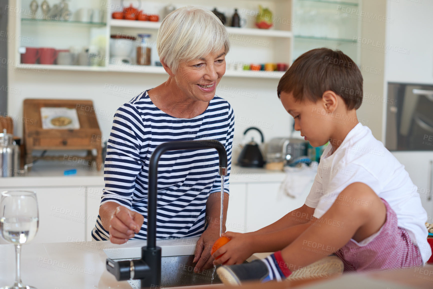 Buy stock photo Cropped shot of a grandmother washing vegetables with her grandchild in a kitchen