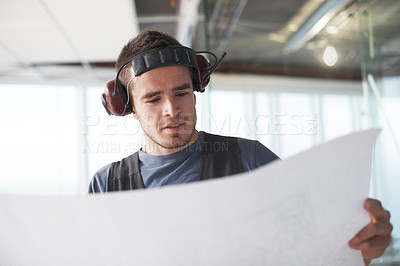 Buy stock photo Young contractor checking his plans on a construction site indoors