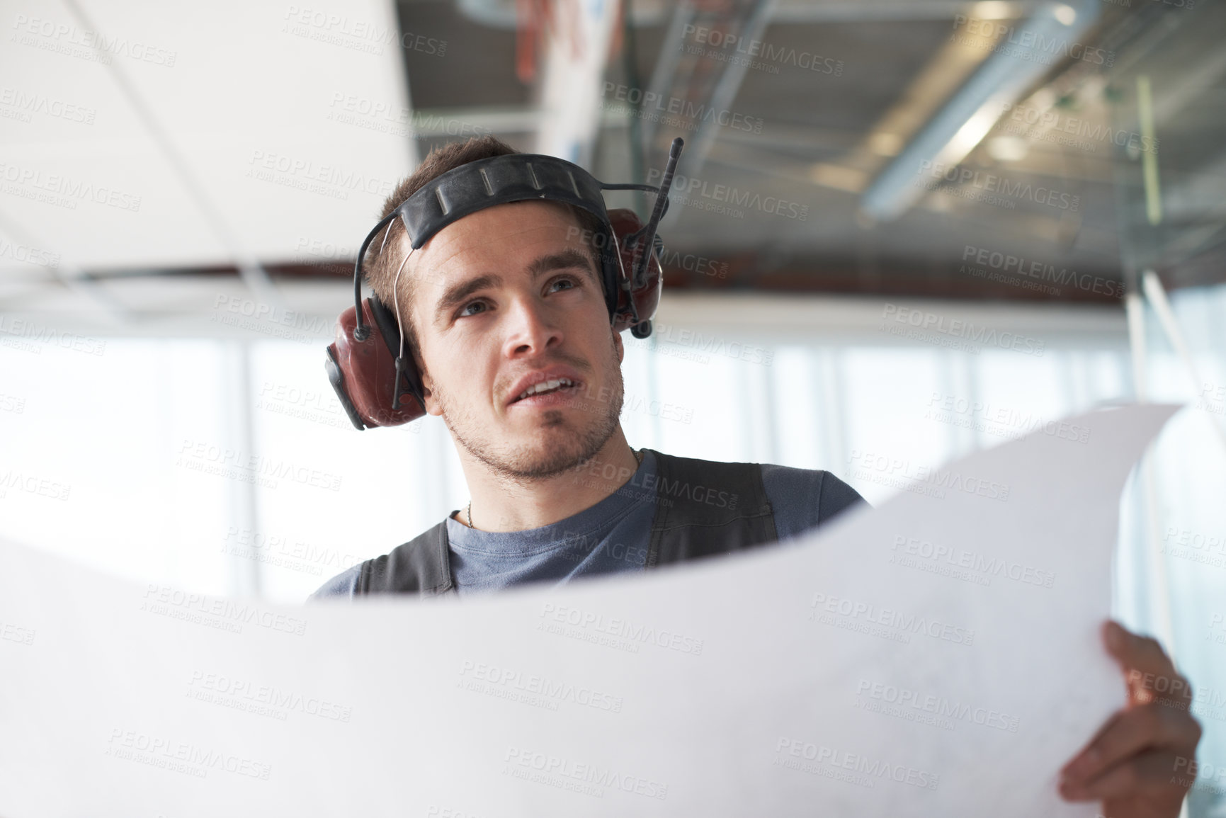 Buy stock photo Young contractor checking his plans on a construction site indoors