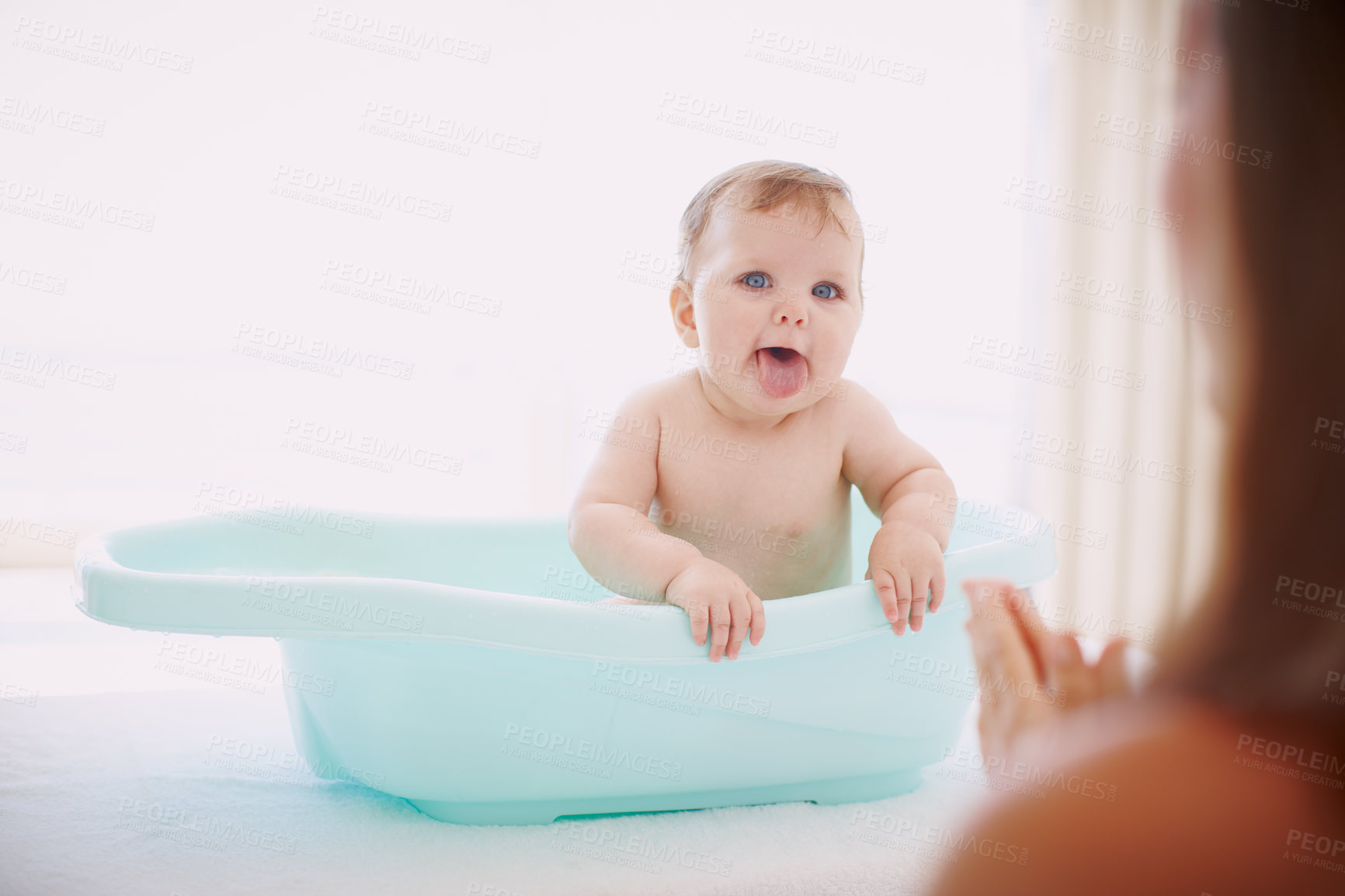 Buy stock photo A baby girl having fun in the bathtub while her mom stands by