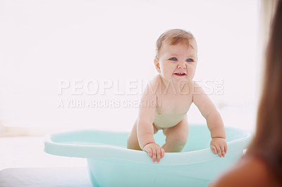 Buy stock photo A baby girl trying to get out of the bathtub while her mom stands by