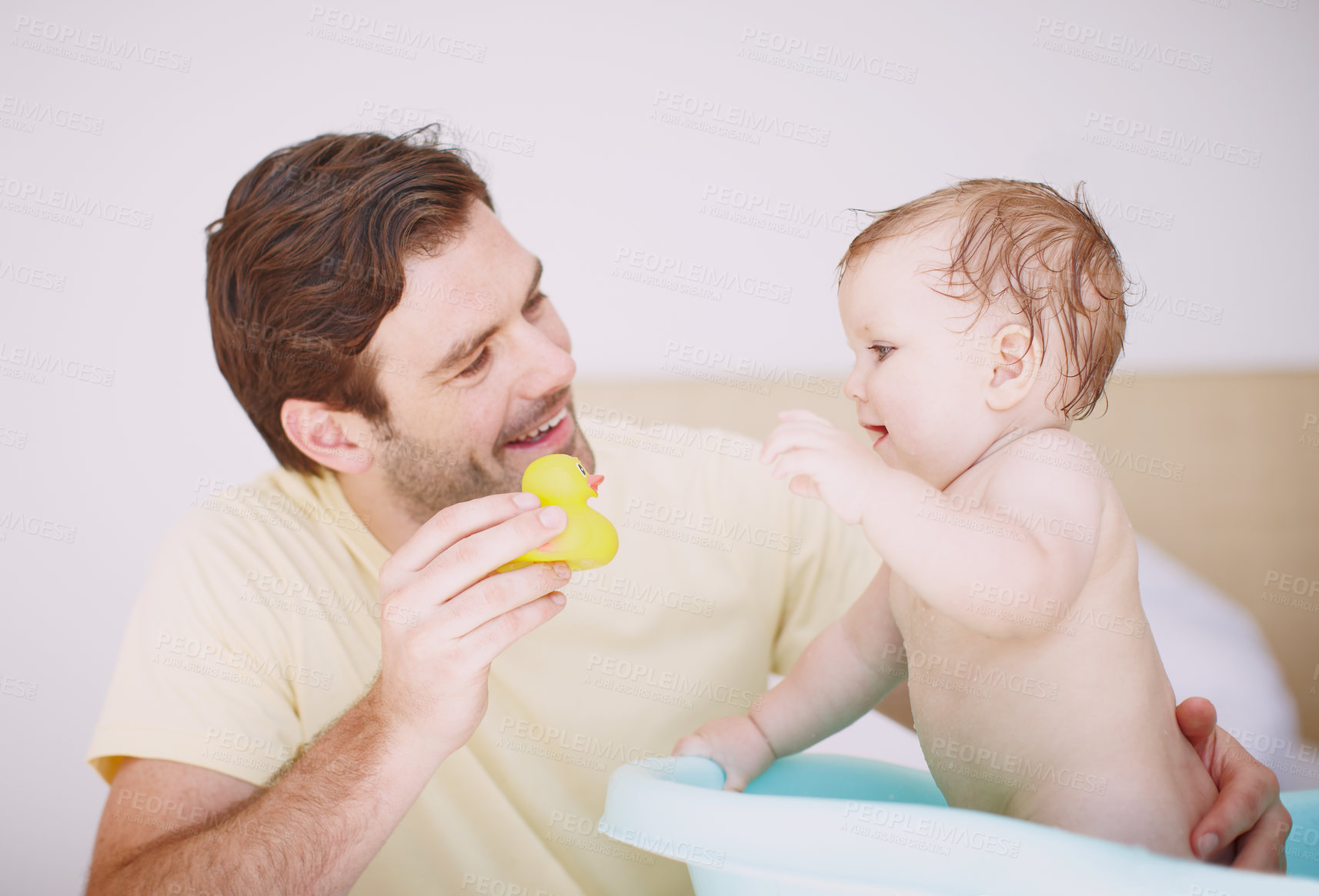 Buy stock photo A young father showing his baby girl a toy while she's in the bathtub