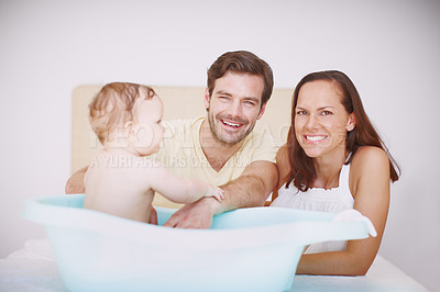 Buy stock photo Portrait of two joyful parents bonding with their baby daughter at bathtime