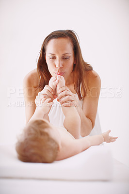 Buy stock photo A young mother showing her baby daughter affection by kissing her toes