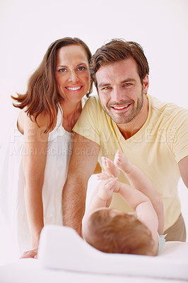 Buy stock photo Portrait of two loving parents standing over their baby daughter as she lies on a changing table