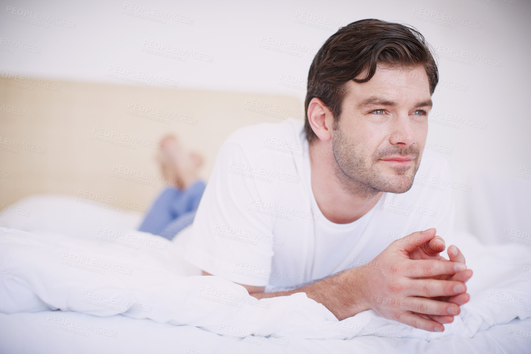 Buy stock photo A handsome young man lying on his stomach on a bed looking thoughtful