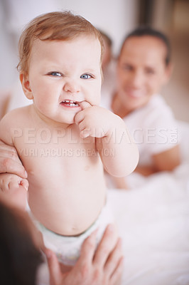 Buy stock photo Cropped shot of a baby girl standing with her thumb in her mouth- family in background