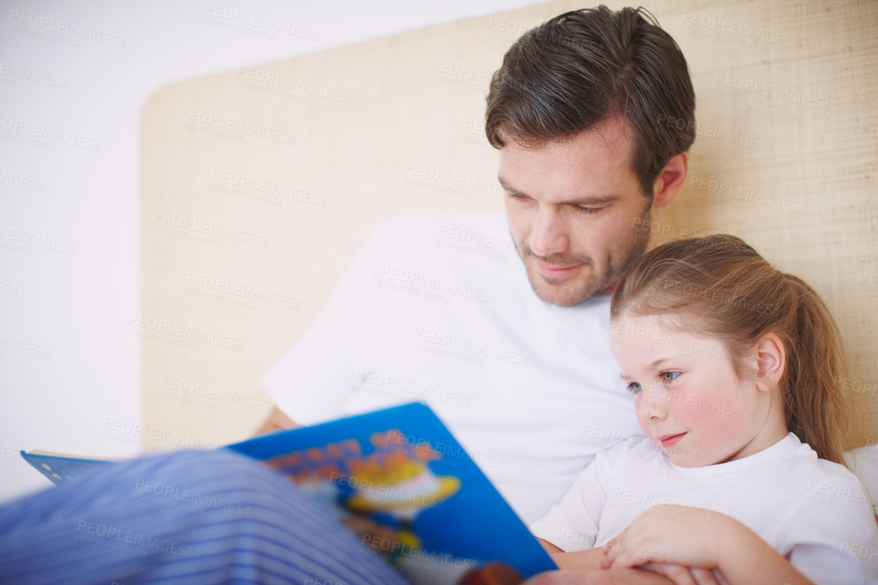 Buy stock photo A devoted father reading his young daughter a bedtime story