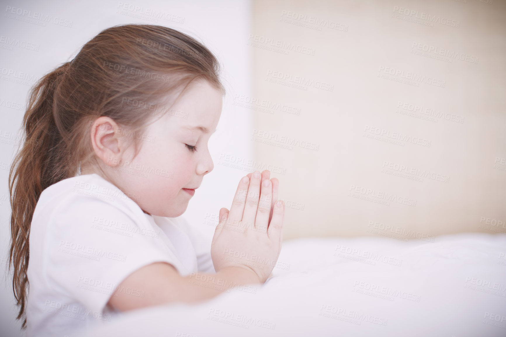 Buy stock photo Side view of a young girl kneeling by her bed and saying her prayers. Little girl joining her hands and praying alone before bed in her bedroom at home. Child practicing her religious beliefs
