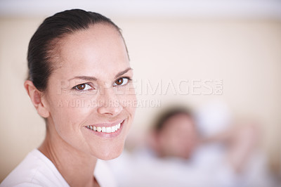 Buy stock photo Shot of an attractive young woman in a bedroom with her husband lying in the background
