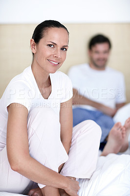 Buy stock photo Portrait of a smiling young woman sitting on a bed with her husband in the background