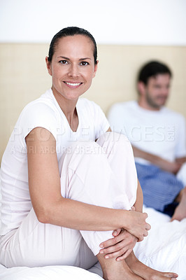 Buy stock photo A young woman sitting on a bed with her husband in the background