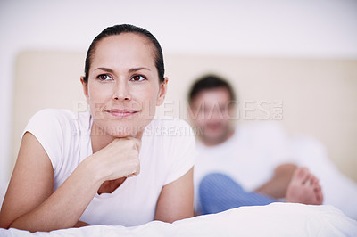 Buy stock photo A young woman lying on a bed with her husband in the background