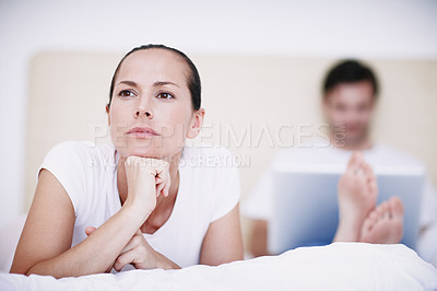 Buy stock photo A young woman looking displeased with her husband who is sitting in the background with his laptop