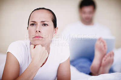 Buy stock photo A young woman looking displeased with her husband who is sitting in the background with his laptop