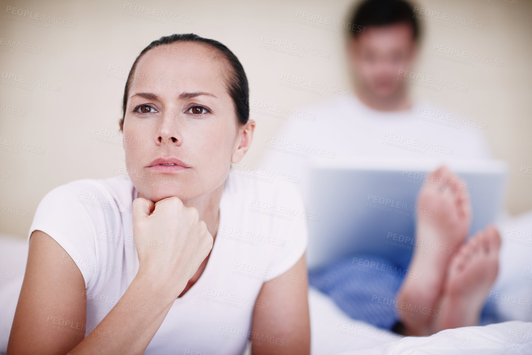 Buy stock photo A young woman looking displeased with her husband who is sitting in the background with his laptop