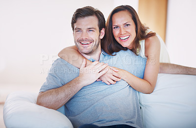 Buy stock photo A loving young wife embracing her husband from behind while he sits on a sofa