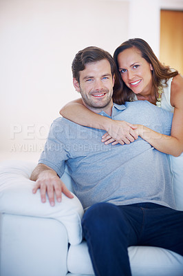 Buy stock photo A loving young wife hugging her husband from behind while he sits on a sofa