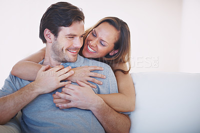Buy stock photo A loving young wife showing her husband affection while he sits on a sofa