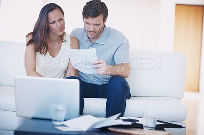 Buy stock photo A young couple discussing their home finances and inspecting bills while sitting together in their living room