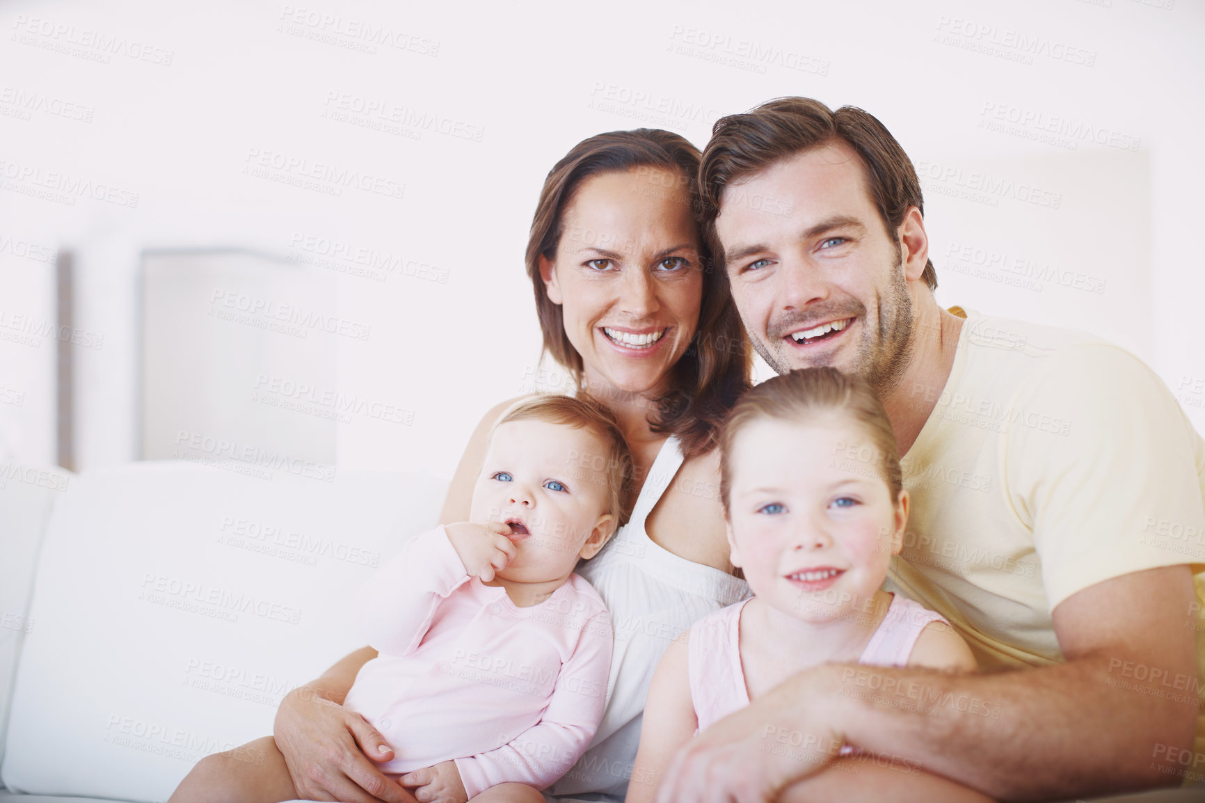 Buy stock photo Cropped portrait of a happy family of four sitting close together on a sofa indoors 