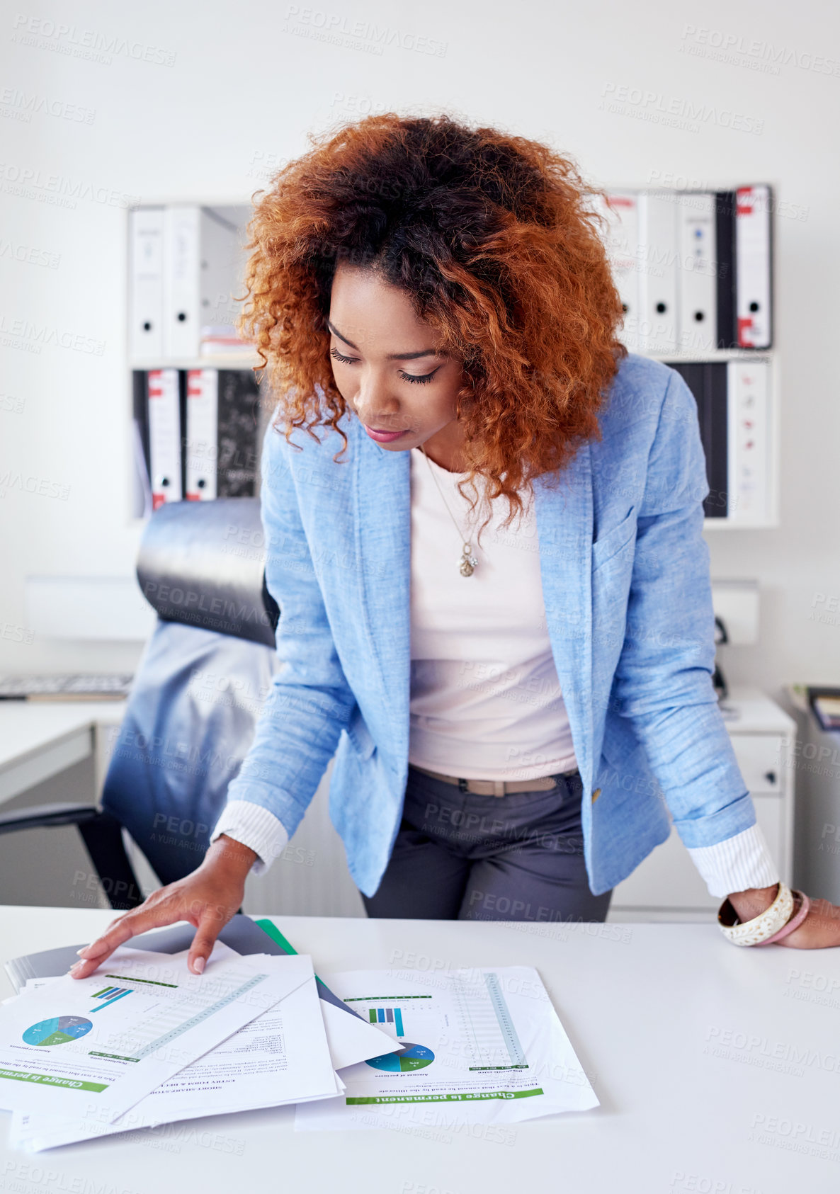 Buy stock photo Shot of a young businesswoman going over paperwork at her office desk