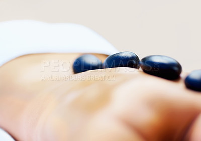 Buy stock photo Back, stone massage and person at spa for wellness, holistic therapy or relax in studio on brown background. Beauty salon, skincare and closeup of client with detox rocks for healing muscle treatment