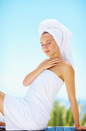 Relaxed female wrapped in a towel sitting against the blue sky