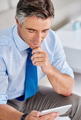 Buy stock photo Shot of a mature businessman using a tablet while sitting on a sofa