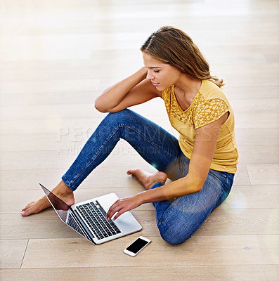 Buy stock photo Shot of a young woman sitting on the floor with her cellphone and laptop