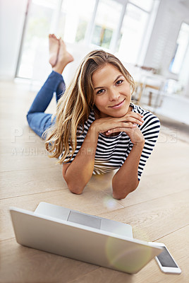 Buy stock photo Shot of a young woman lying on the floor with her cellphone and laptop