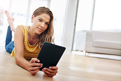 Buy stock photo Shot of a young woman lying on her living room floor with her digital tablet