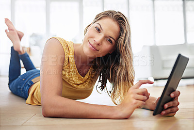 Buy stock photo Shot of a young woman lying on her living room floor with her digital tablet