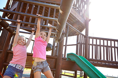 Buy stock photo Shot of two little girls hanging on the monkey bars at the playground