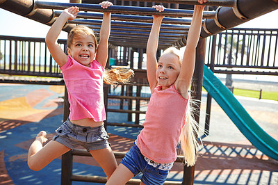 Buy stock photo Shot of two little girls hanging on the monkey bars at the playground