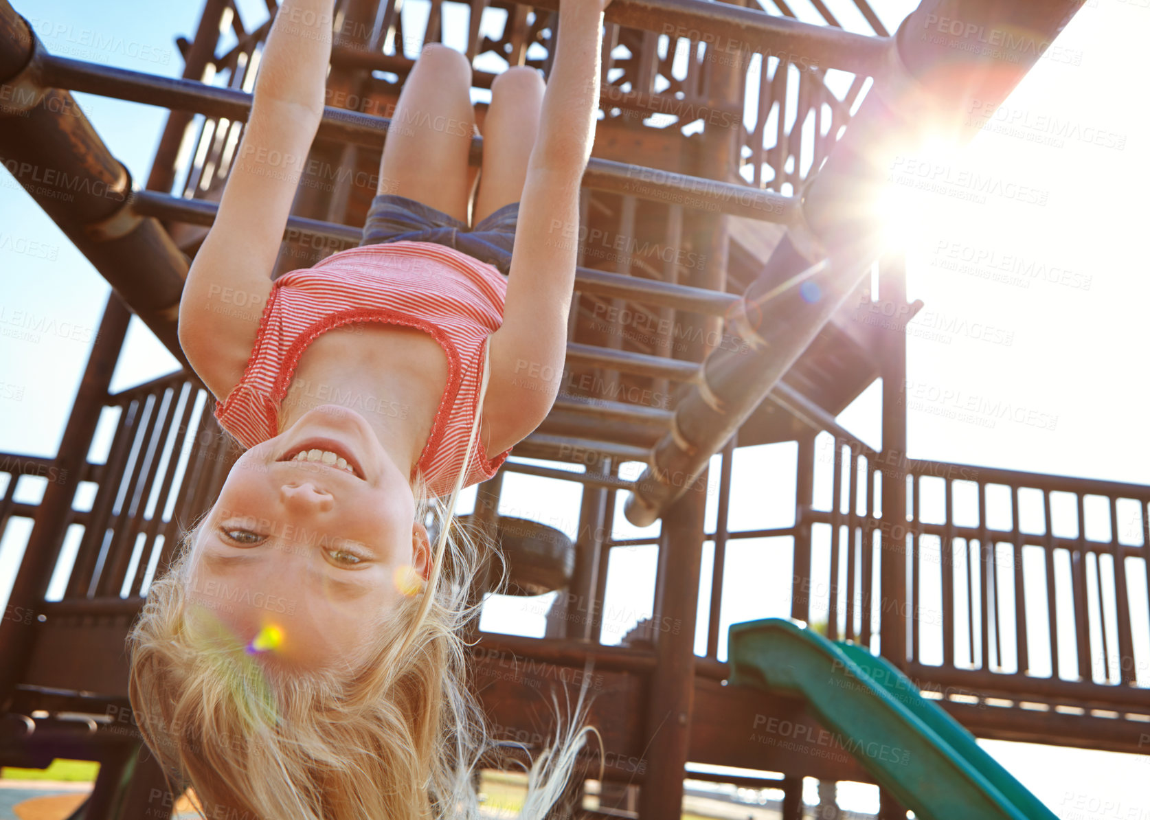 Buy stock photo Shot of a little girl hanging upside down on monkey bars at the playground