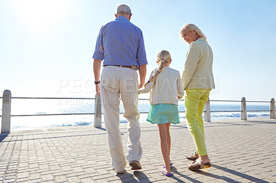 Buy stock photo Shot of grandparents walking hand in hand with their granddaughter on a promanade