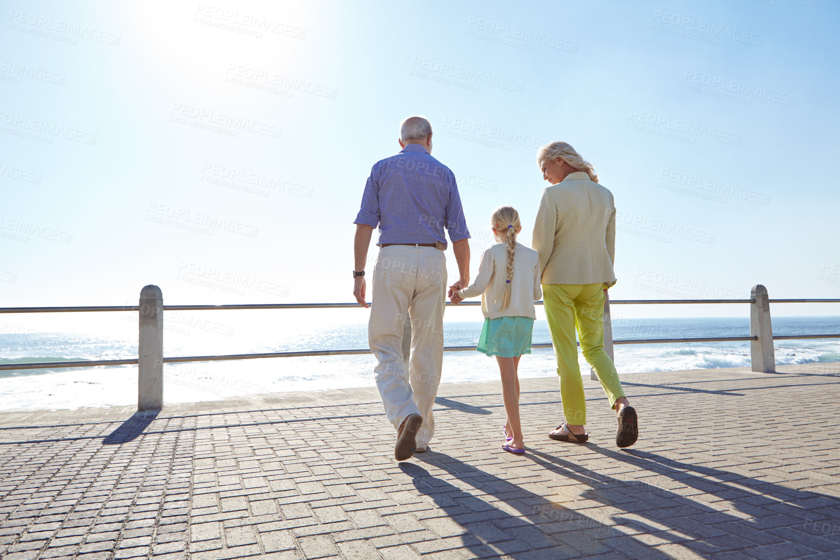 Buy stock photo Shot of grandparents walking hand in hand with their granddaughter on a promanade