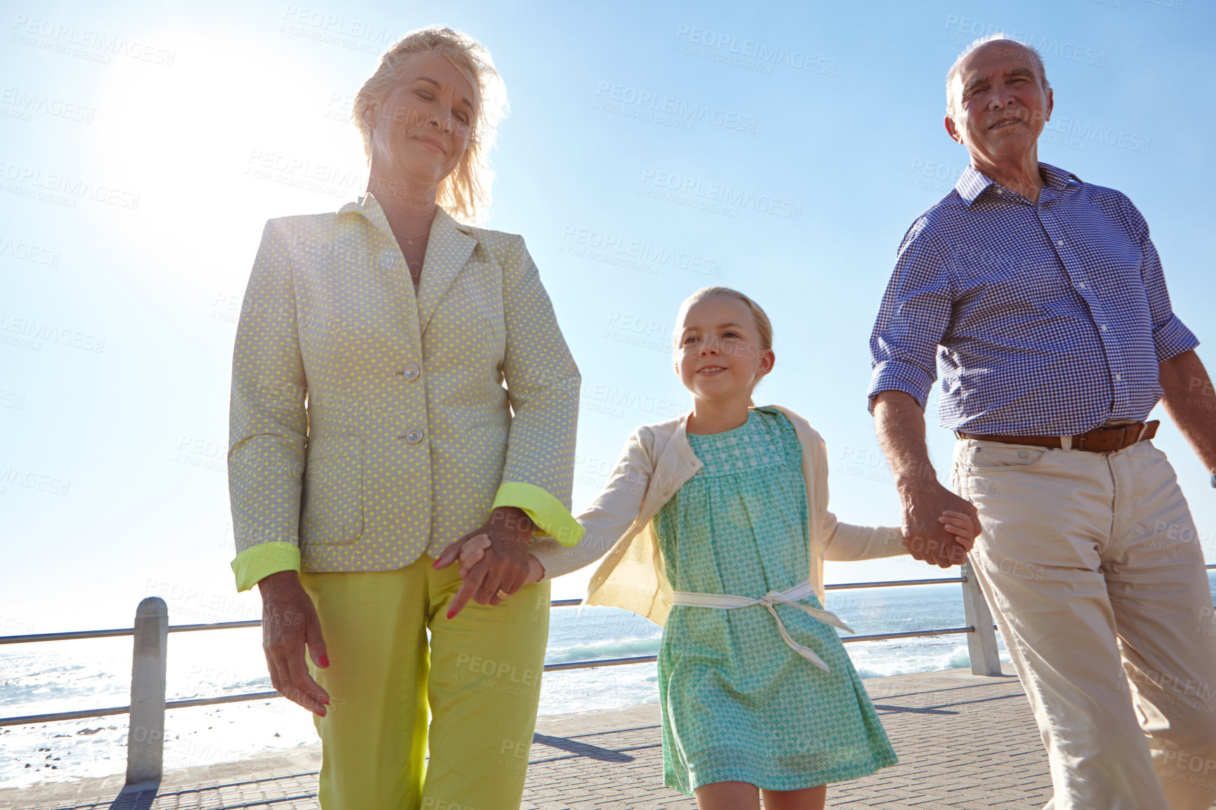 Buy stock photo Shot of grandparents walking hand in hand with their granddaughter on a promanade