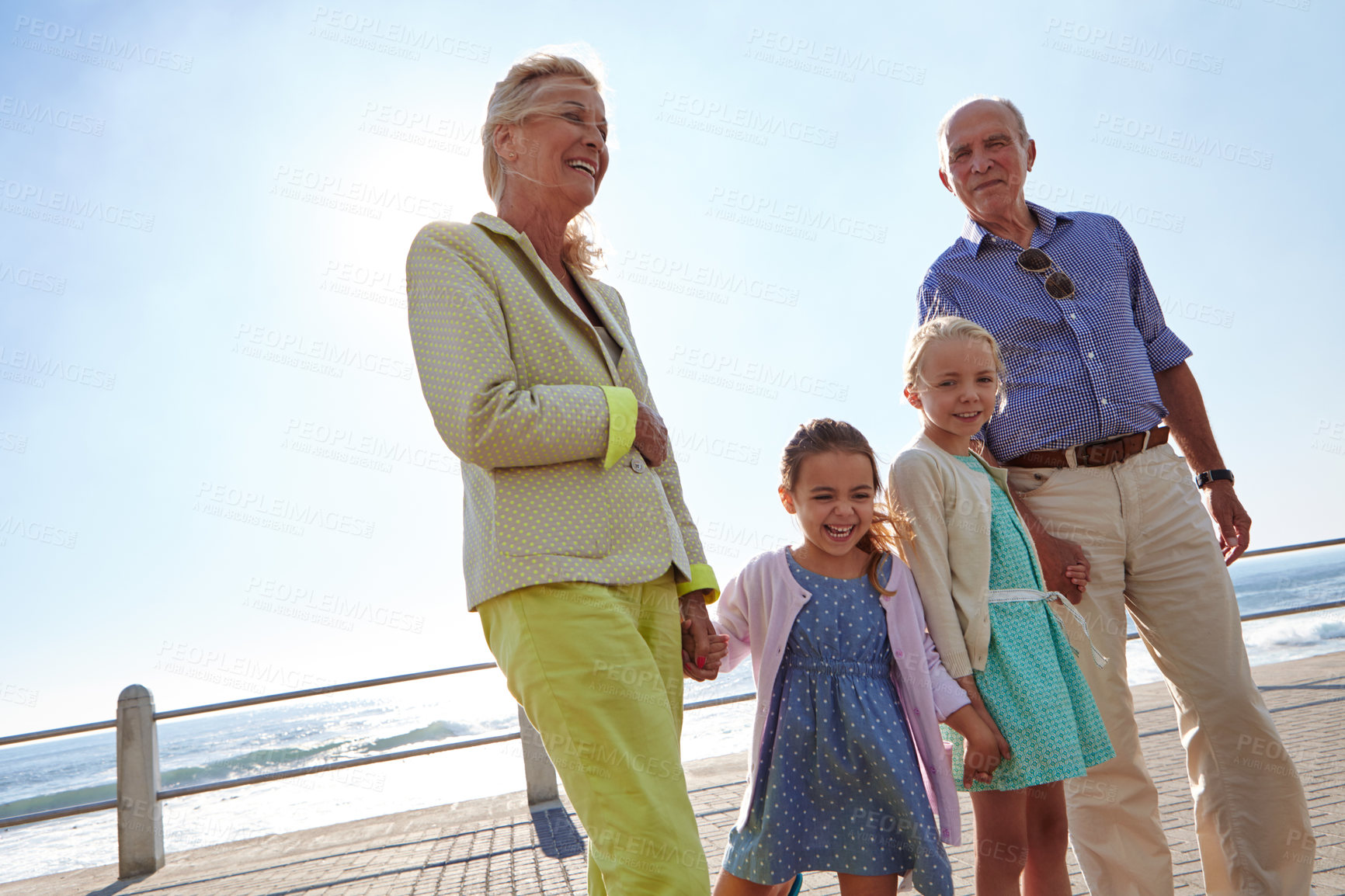 Buy stock photo Shot of grandparents walking hand in hand with their granddaughters on a promanade