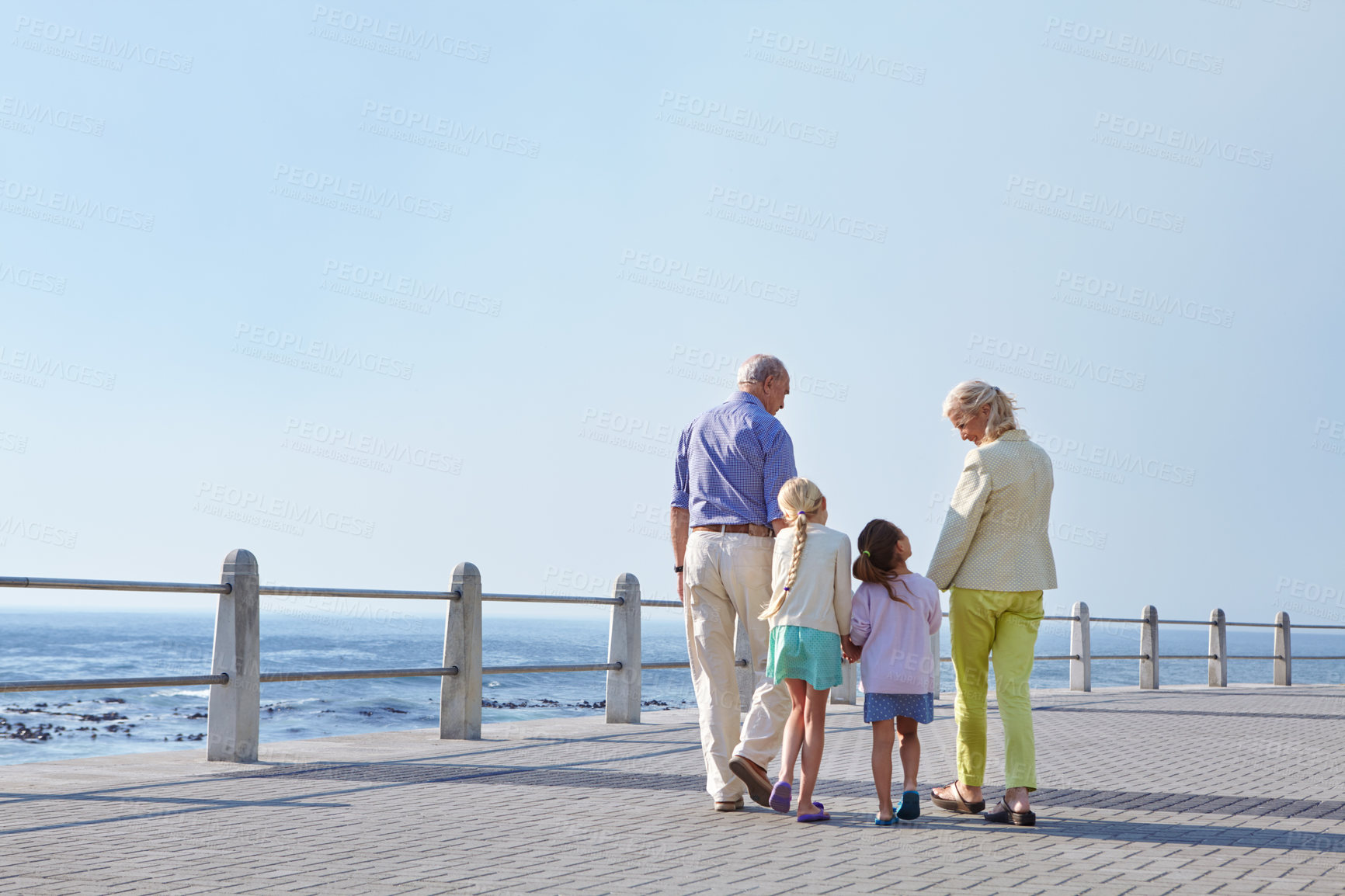 Buy stock photo Shot of grandparents walking hand in hand with their granddaughters on a promanade